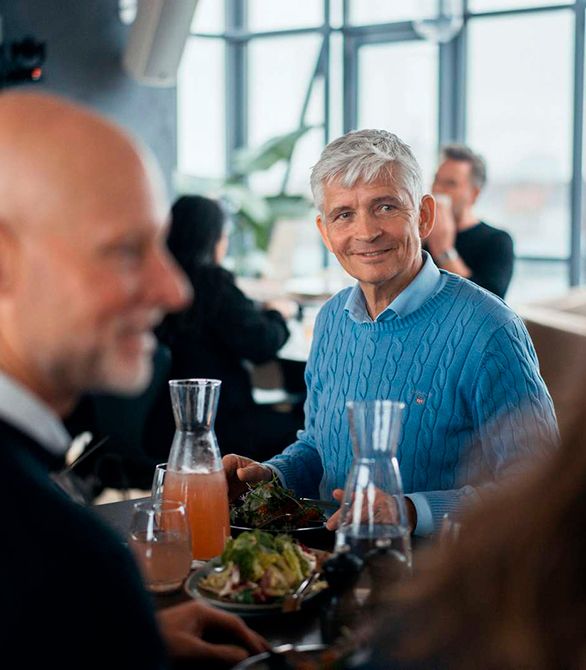 En ældre gråhåret mand sidder og spiser mad sammen med andre mennesker